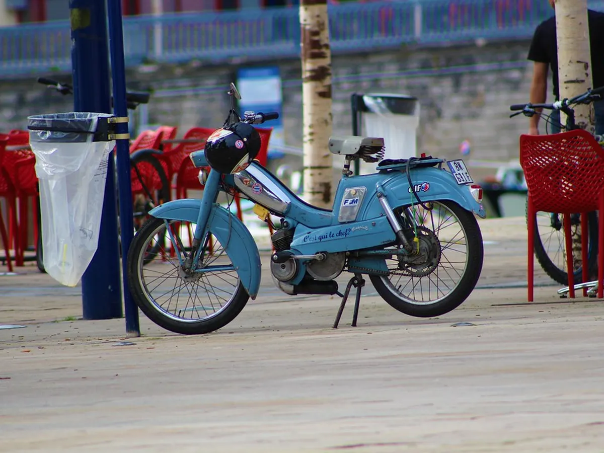 Ciclomotor azul clásico aparcado junto a una terraza